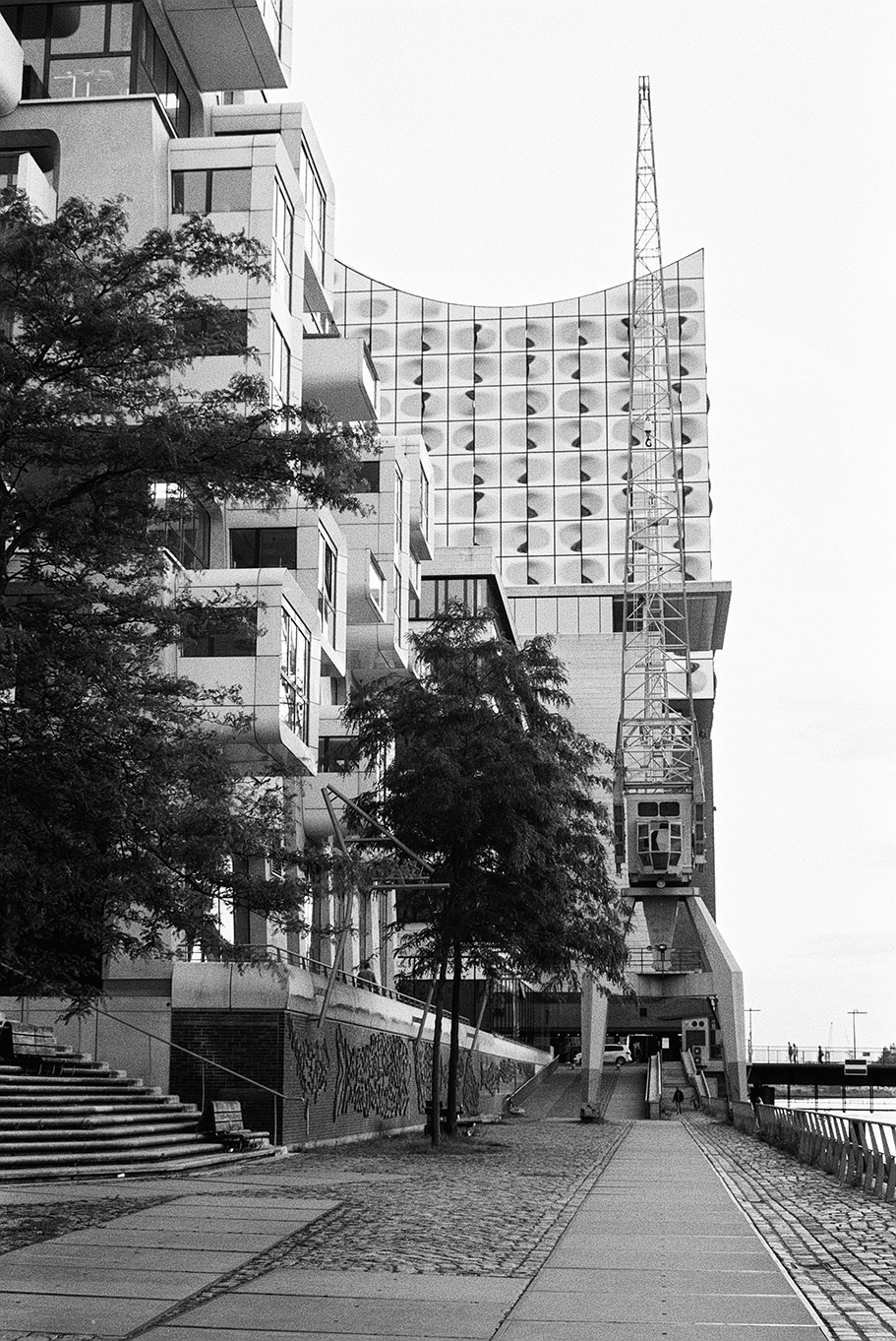 The backside of the Elbphilhamonie in Hamburg with an old cargo crane and apartments in front of it. Shot in Ilford Delta 100