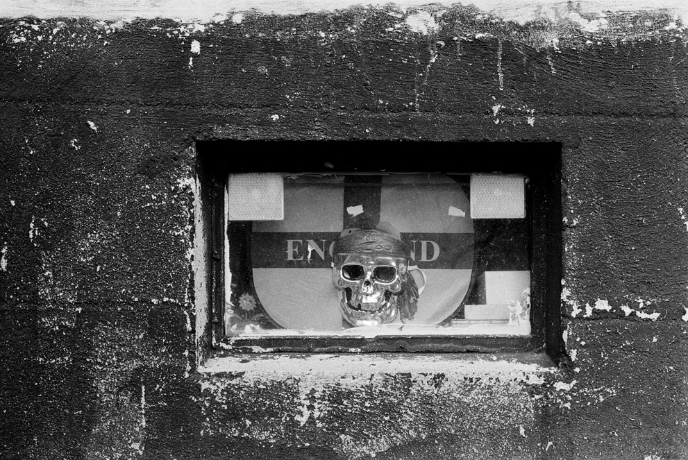 Flag of England with a silver skull in a dirty basement window. Shot on Kodak Tri-X 400.